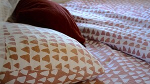 Ein Bett mit gemusterten Betttextilien und einem roten Kissen.
