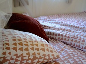 Un letto con biancheria a motivi e un cuscino rosso.