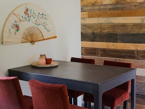 Un'area pranzo con un tavolo in legno scuro, sedie imbottite rosse e una ventaglio decorativo con motivo floreale sulla parete.