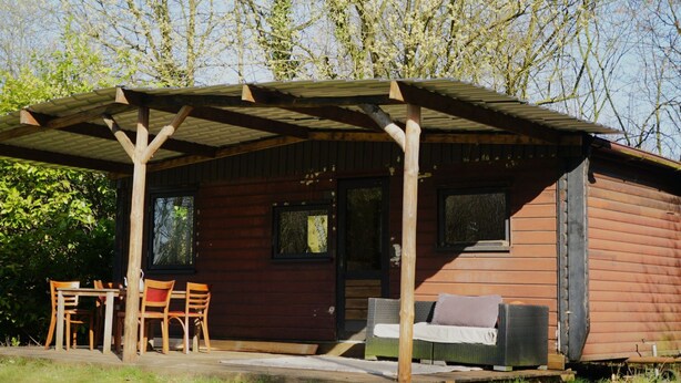 Eine Holzdiele mit überdachter Veranda, einem Esstisch mit Stühlen und einem Sofa.