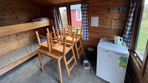 L’intérieur d’un chalet en bois comprend des lits superposés, une table à manger, des chaises, un réfrigérateur et une fenêtre avec des rideaux.