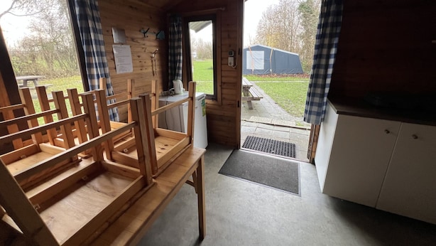 Un intérieur en bois avec un banc, une porte donnant sur l’extérieur et une vue sur un espace verdoyant.