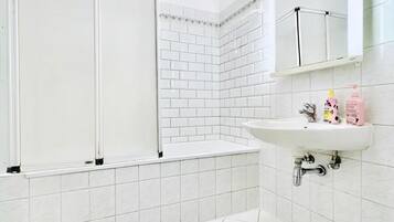 A bathroom with white tiles, a shower enclosure, a sink, and a mirror.