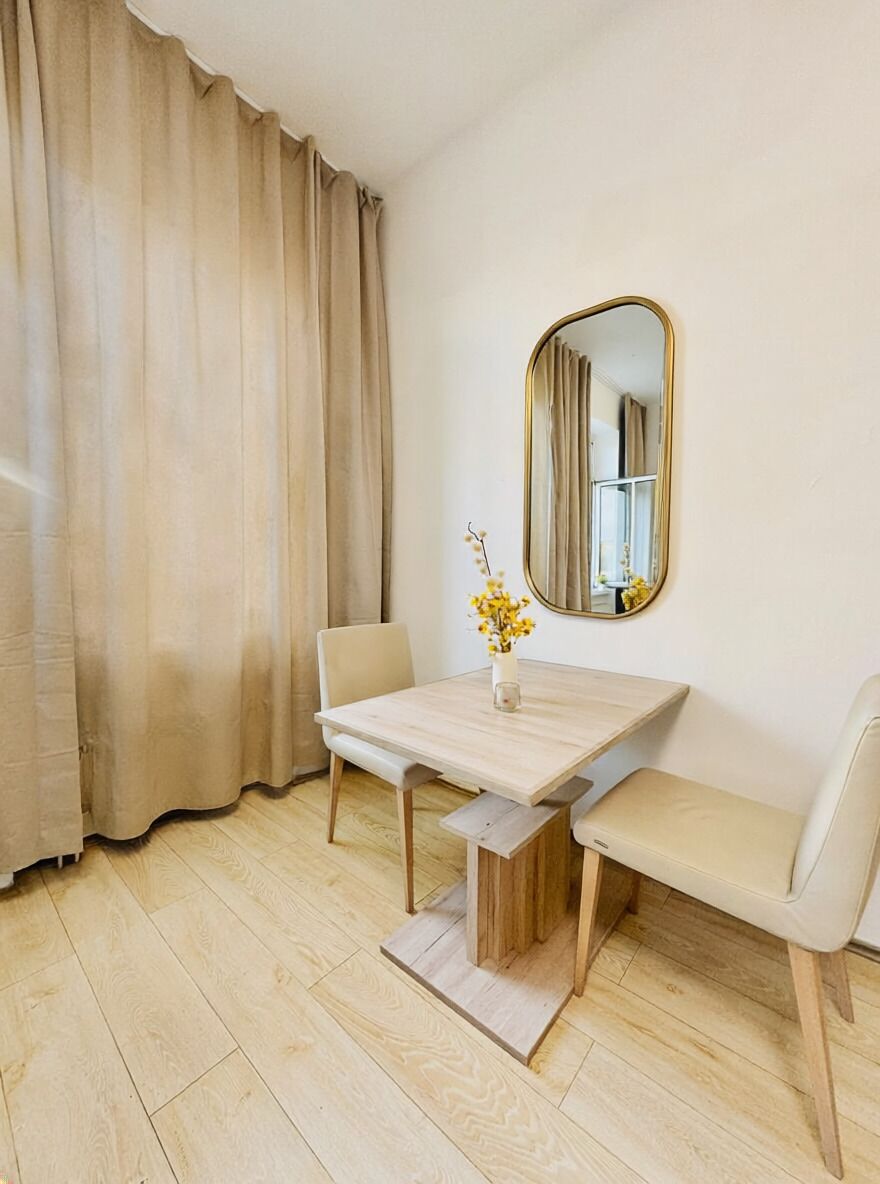 A room with a wooden table, two chairs, a bench, a mirror, and a window with curtains.
