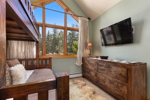 Ein Zimmer mit einem hölzernen Bett, einem Holzschrank, einem an der Wand montierten Fernseher und einem großen Fenster mit Vorhängen.