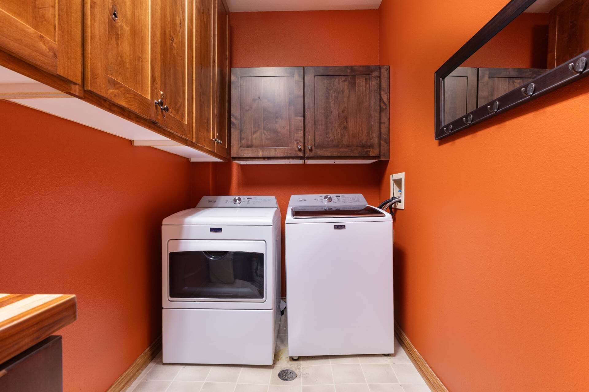 A laundry room with two white washing machines, wooden cabinets, and an orange wall.