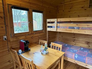 Interno di una baita in legno con un letto a castello, un tavolo con sedie, una moka e una finestra con persiane.