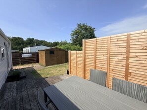 A patio area with a wooden table and chairs, a wooden fence, and a small shed. - Vakantiepark de Nollen - L001 by Interhome (Callantsoog)