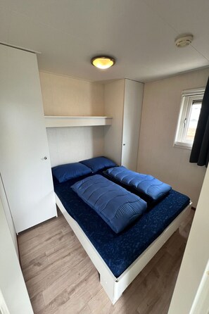 A compact room with a bed, a wardrobe, a ceiling light, and a window. - Vakantiepark de Nollen - L001 by Interhome (Callantsoog)