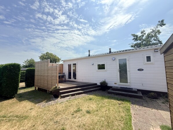 A mobile home with a patio, a small deck, and a fenced yard. - Vakantiepark de Nollen - L001 by Interhome (Callantsoog)