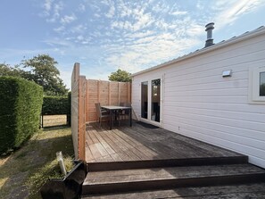 A covered patio with a table and chairs, a wooden fence, and a white building with a chimney. - Vakantiepark de Nollen - L001 by Interhome (Callantsoog)