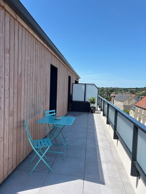 En balkon med et bord og stole, en potteplante og udsigt over bybilledet.
