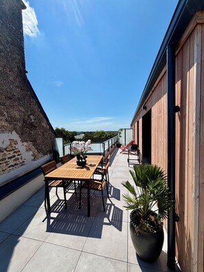 Eine Dachterrasse mit Holztisch und -stühlen, Blumentöpfen und Blick auf die Umgebung.