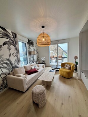 A modern living room with a sofa, a yellow armchair, a coffee table, and a hanging light fixture. - The Riva rooftop—like a house perched on a roof. (Barneville-Carteret)