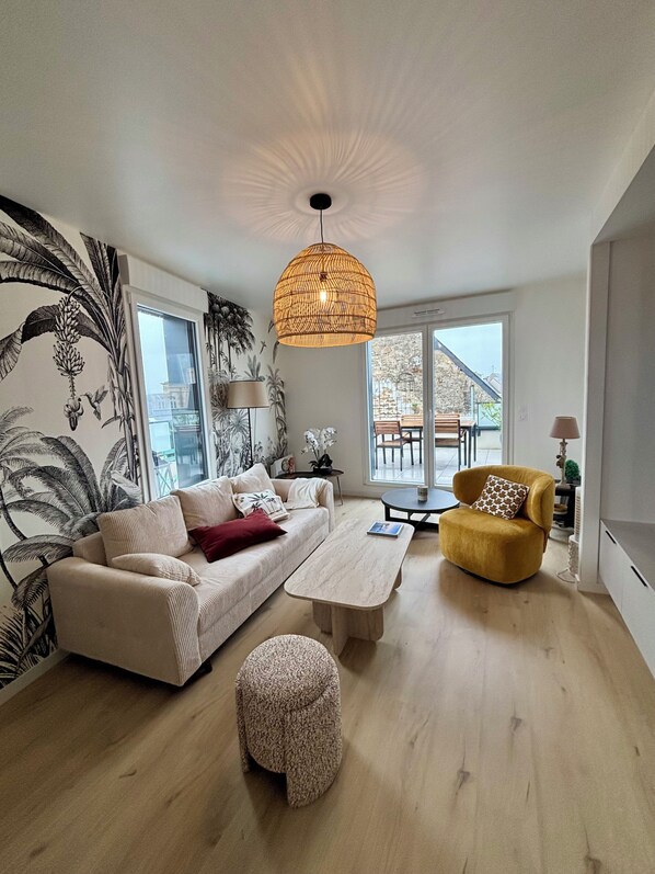 En moderne stue med sofa, gul lænestol, sofabord og en hængende lampe.