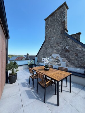 Eine Dachterrasse mit Holztisch und -stühlen, Blumentöpfen und einer Steinmauer.