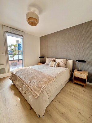 Ein modernes Schlafzimmer mit einem großen Bett, einem Nachttisch mit Lampe und Blick durch eine Schiebetür.