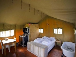 Een tentaccommodatie met een bed, een klein bureau, een stoel, een wastafel en een raam.