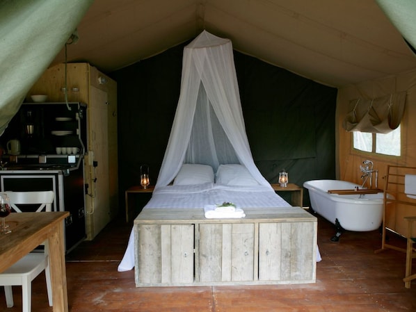 Een tentaccomodatie met een bed, een tafel, een wastafel en een kleine kitchenette.