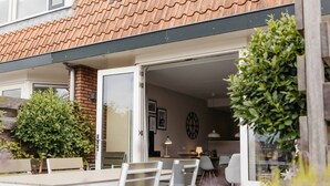 A modern outdoor dining area with a table and chairs, a brick wall, and a glass door leading to an interior space.