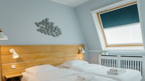 A hotel room with a wooden headboard, two beds, a wall-mounted light fixture, and a window with blinds.