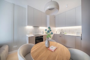A modern kitchen with a round dining table, a vase with flowers, and a pendant light. - Kierbedzia Beige Elagant, Mokotow, Warsaw (Warszawa)