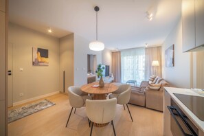A modern living room with a round dining table, sofas, and a kitchen area. - Kierbedzia Beige Elagant, Mokotow, Warsaw (Warszawa)