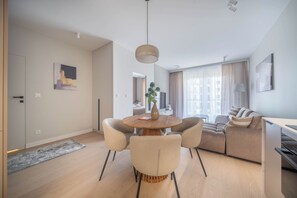 Un salon moderne avec une table à manger ronde en bois, des canapés beige et une grande fenêtre avec des rideaux.