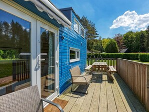 A blue house with a deck, a glass door, and a wooden fence. - De Glamping - Blauwe Tiny House | 6p by Interhome (Zeewolde)