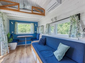 A cozy interior with a blue sofa, a small table, and a bench area. - De Glamping - Blauwe Tiny House | 6p by Interhome (Zeewolde)