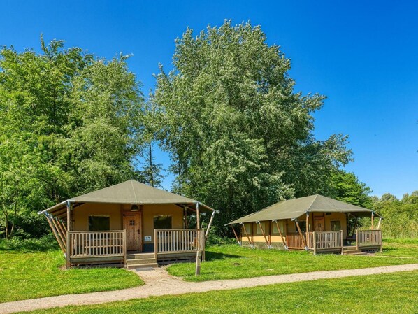 Two small, single-story cabins with a porch and a door, surrounded by a grassy area and trees. - De Glamping - Duo Lodge | 12p by Interhome (Zeewolde)