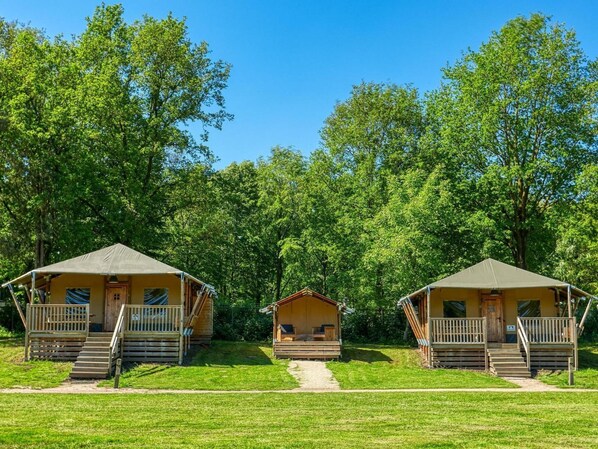 Three wooden cabins with balconies, set in a forest with a clear sky. - De Glamping - 2 1/2 family combo by Interhome (Zeewolde)