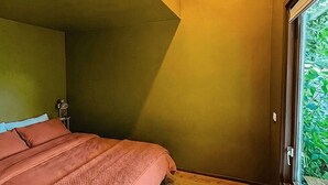 Ein Schlafzimmer mit einem Bett, einem Nachttisch und einem Fenster mit Blick auf Grünflächen.