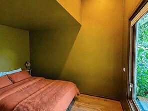 A bedroom with a bed, a nightstand, and a window with a view of greenery. - Camping Ont Moeten - Hallertau by Interhome (Rekken)