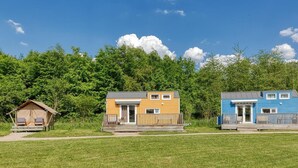 Una filera de tres cabanes amb primer un prat i al fons un bosc.