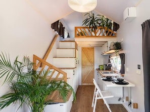A compact kitchen with a wooden staircase, a dining area, and a small seating space. - De Glamping - Gele Tiny House | 5p by Interhome (Zeewolde)