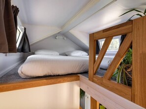 A small, cozy bedroom with a single bed, a window, and a view of the outdoors. - De Glamping - Gele Tiny House | 5p by Interhome (Zeewolde)