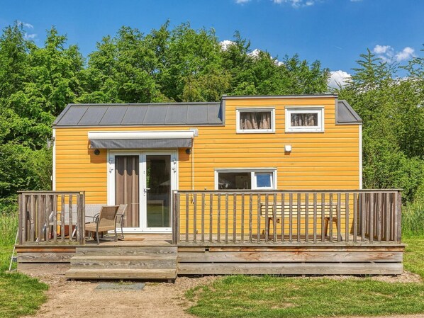 A yellow two-story building with a deck, a door, and a window. - De Glamping - Gele Tiny House | 5p by Interhome (Zeewolde)