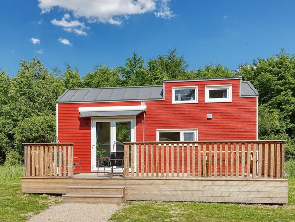 A red wooden house with a front deck, a sliding glass door, and a small porch. - De Glamping - Tiny House rood | 5p by Interhome (Zeewolde)