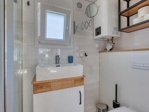 A bathroom with a white sink, a mirror, a window, and a towel rack. - De Glamping - Tiny House rood | 5p by Interhome (Zeewolde)