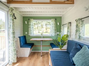 A cozy interior with a green wall, a wooden table, a bench, and a sofa. - De Glamping - Tiny Safari Groen | 8p by Interhome (Zeewolde)