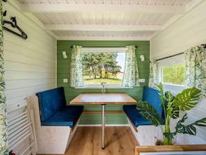 A compact room with a green wall, a window with curtains, a table, and two blue cushioned seats. - De Glamping - Tiny Safari Groen | 8p by Interhome (Zeewolde)