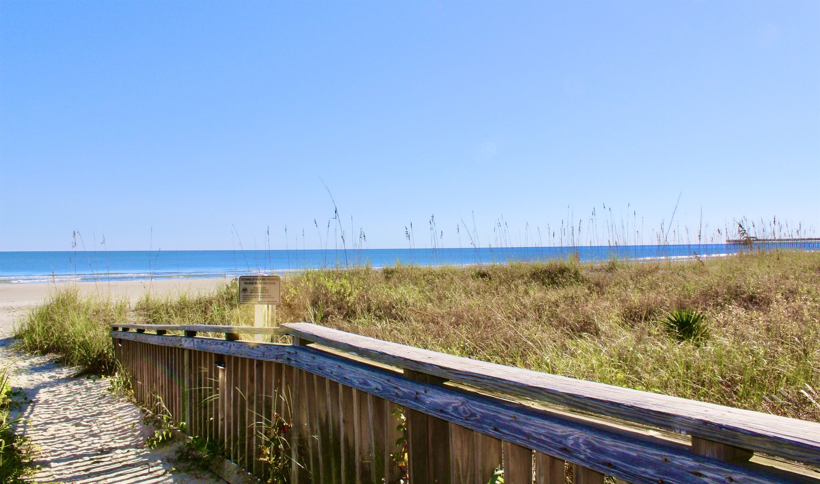 A wooden boardwalk leading to a beach with a clear view of the ocean.