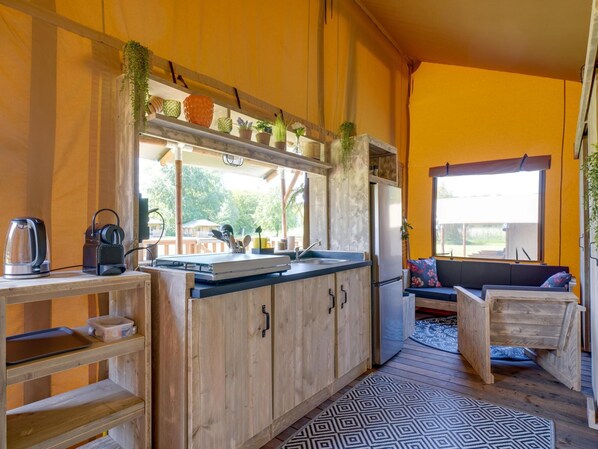 A compact kitchen with wooden cabinets, a countertop, and a window overlooking a deck. - De Glamping - Sunny Lodge | 6p by Interhome (Zeewolde)