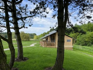 A small cabin with a deck, surrounded by trees and a grassy field. - De Glamping - Sunny Lodge | 6p by Interhome (Zeewolde)