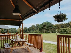 An outdoor wooden deck with picnic tables and hanging plants. - De Glamping - Glamping Lodge | 5p by Interhome (Zeewolde)