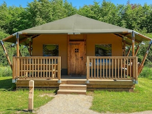 A single-story wooden structure with a porch and a door, surrounded by greenery. - De Glamping - Glamping Lodge | 5p by Interhome (Zeewolde)
