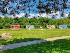 A row of colorful cabins in a grassy field with a clear sky. - De Glamping - Groene Tiny House | 6p by Interhome (Zeewolde)
