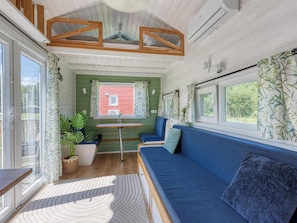 A cozy interior with a blue sofa, a small table, and a window with curtains. - De Glamping - Groene Tiny House | 6p by Interhome (Zeewolde)
