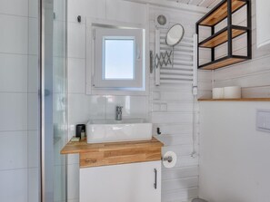 A bathroom with a white sink, a mirror, and a wooden shelf. - De Glamping - Trio Tiny Houses & Safaritent | 14p by Interhome (Zeewolde)